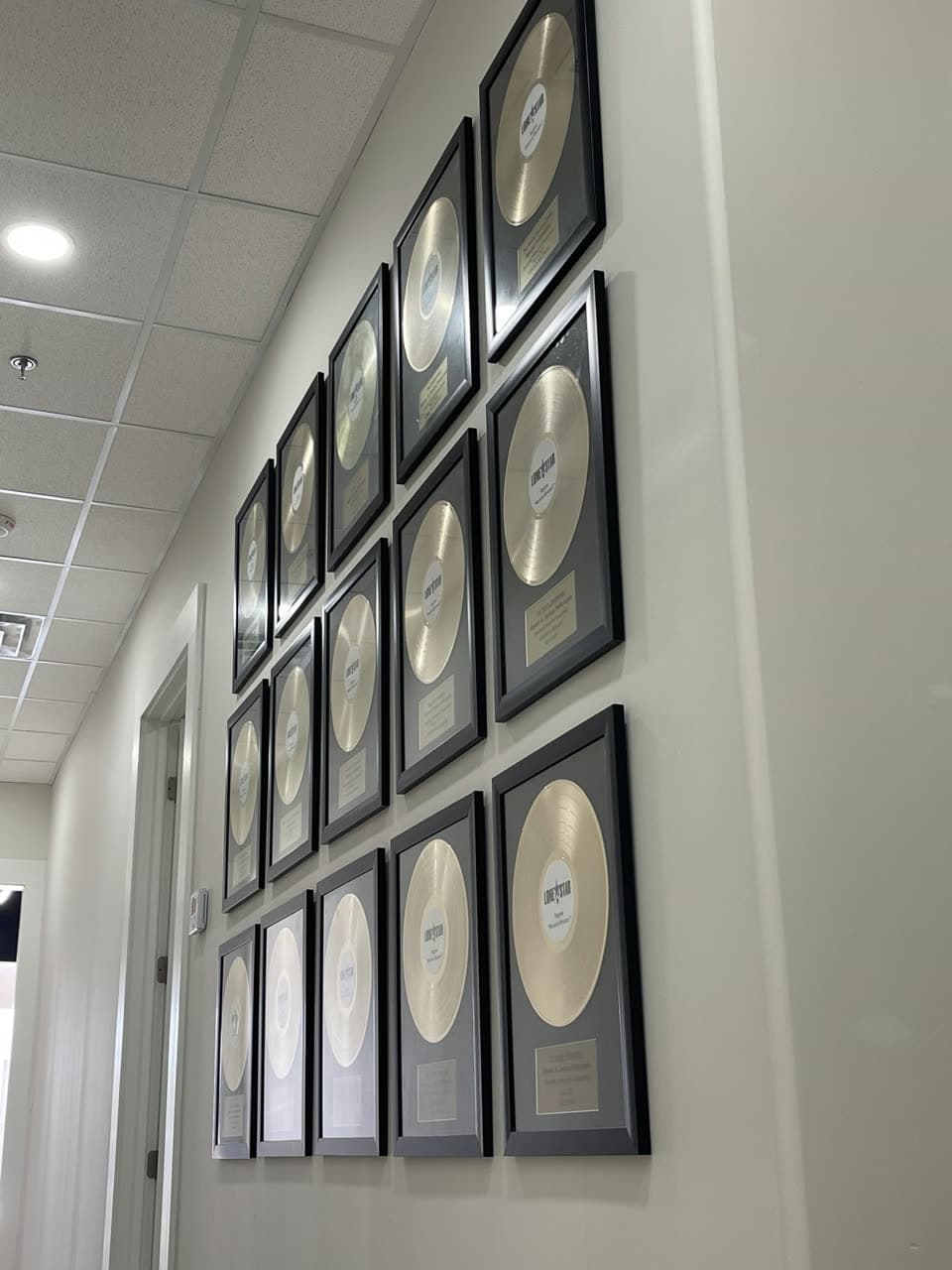 Office corridor wall hung with rows of framed gold and platinum records in black frames.