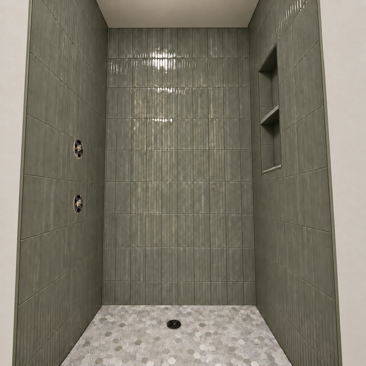 Shower stall tiled in stacked sage green vertical tile with a recessed shelf niche and a pebble mosaic floor.